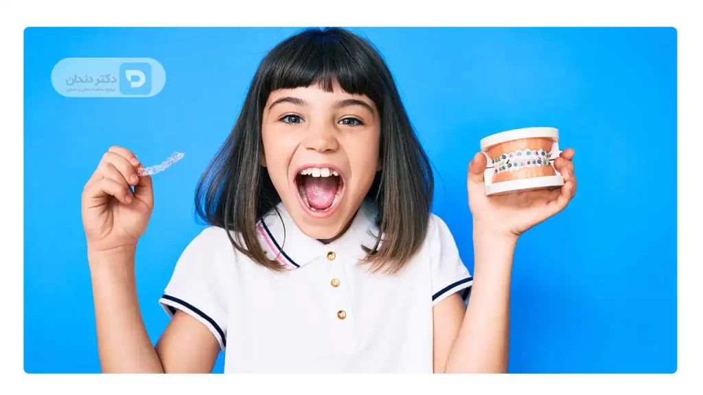 عکس یک کودک که در دست چپش مولاژ فکی که ارتودنسی شده دارد و در دست راستش یک پلاک ارتودنسی نامرئی دارد تصویر نشانگر این است که هزینه ارتودنسی دندان کودکان کمتر است